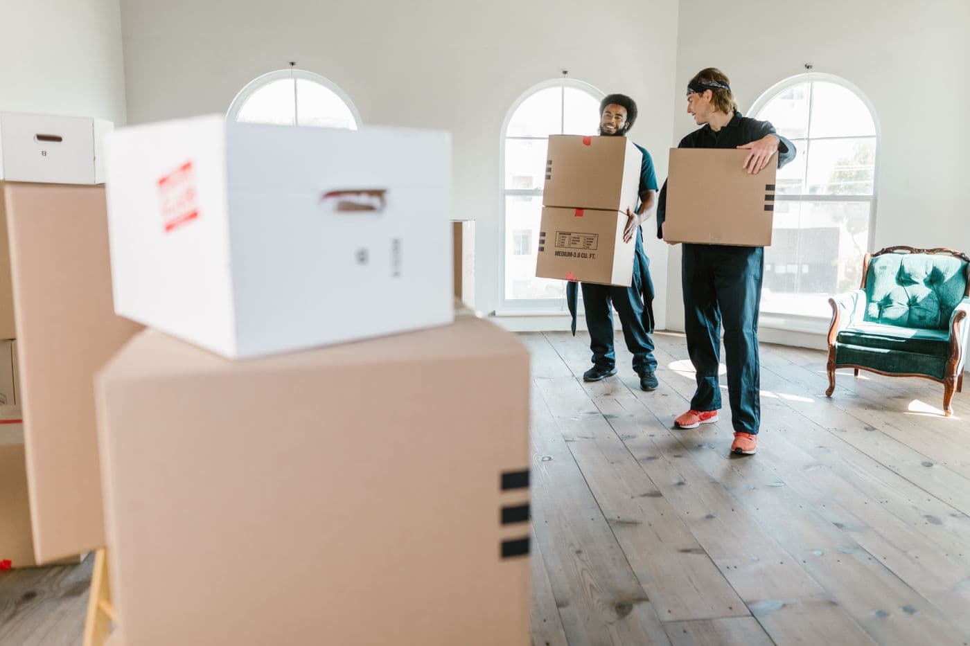Two people carrying packed boxes through a bright room